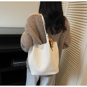 Detail shot of white woven tote bag with colorful beaded charm on a shoulder strap