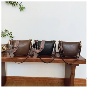 Three retro bucket bags in brown and black with wide patterned shoulder straps on wood