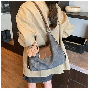 Detail of dark grey canvas hobo bag featuring brown leather flap and cute bear charm