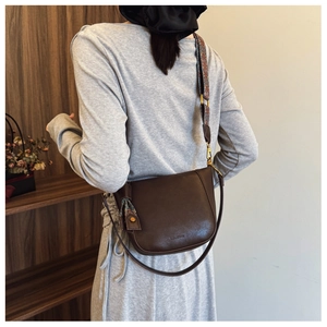 Detail of dark brown leather bucket bag with colorful woven strap and fringe tassel charm
