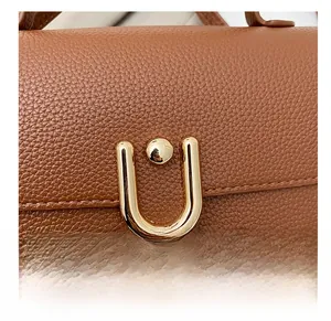 Close-up of brown litchi grain leather texture and gold U-shaped hardware buckle