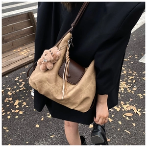 Detail view of khaki canvas tote with brown leather flap and bear charm in autumn setting