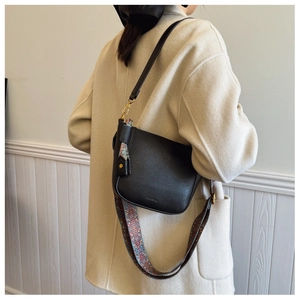 Detail of black leather half-moon bag with ethnic printed wide strap on beige coat