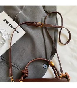 Detail of dark brown leather handbag with knotted handle and adjustable gold buckle strap