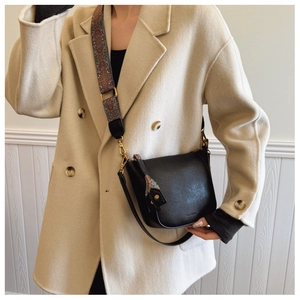 Detail view of black leather bucket bag with vintage patterned wide strap on a beige coat