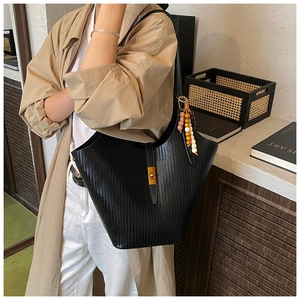 Close-up of black woven texture leather tote bag with gold lock and colorful bead charm