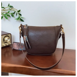 Detail of dark brown leather bucket bag featuring a patterned wide woven shoulder strap