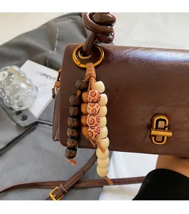 Detail view of brown vintage shoulder bag featuring golden clasp and colorful wood bead tassel