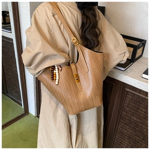 Detail of a brown woven tote bag featuring wooden bead charms and adjustable shoulder strap
