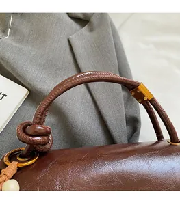 Detail of dark brown leather handbag with knotted handle and golden metal ring