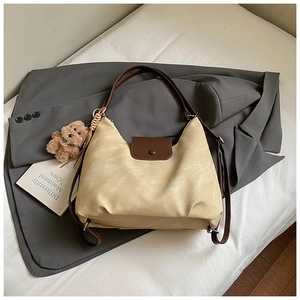 Detail view of cream and brown tote bag showing textured leather and bear charm pendant