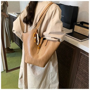 Detail of caramel woven tote bag featuring gold buckle and wooden beaded tassel charm