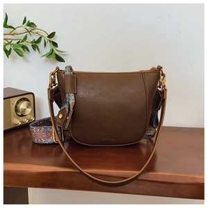 Detail view of brown bucket bag featuring a bohemian style wide woven shoulder strap