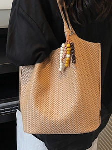 Light brown woven tote bag with beaded charm accessory shown in a shoulder carry style