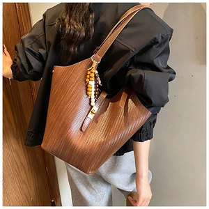 Detail of dark brown tote bag with woven texture, metal buckle and colorful wood bead charm