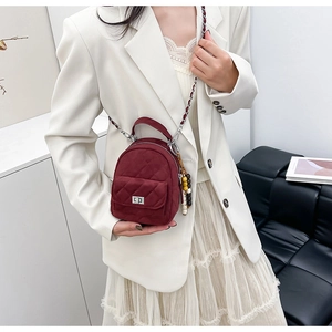 Détail du mini sac à dos matelassé bordeaux avec bandoulière chaîne sur une tenue de blazer