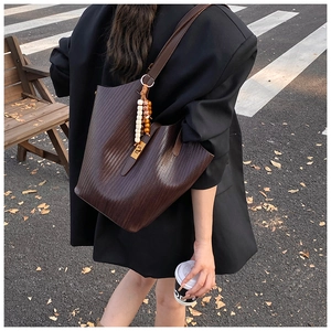 Detail of dark brown woven tote bag featuring stylish beaded pendant and metal clasp