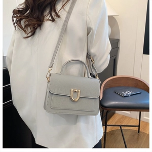 Close-up of light grey litchi grain leather bag with a gold U-shaped metal buckle