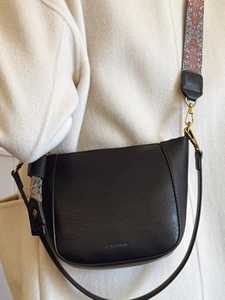 Minimalist black leather bucket bag with vintage printed wide strap on beige wool coat