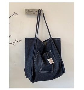 Macro detail of navy denim tote bag featuring white contrast stitching and an outer pocket