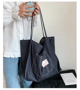 Detail of dark blue denim tote bag showing metal buckle pocket and woven texture