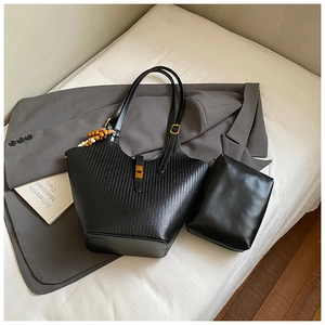 Close-up of black woven tote bag and matching clutch with wood bead accessory and metal buckle