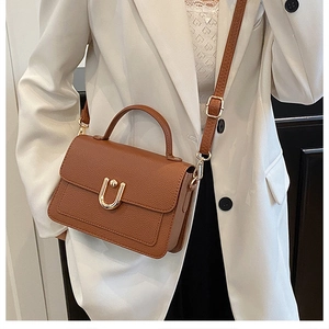 Detail of brown lychee grain leather handbag with gold U-shaped buckle and crossbody strap