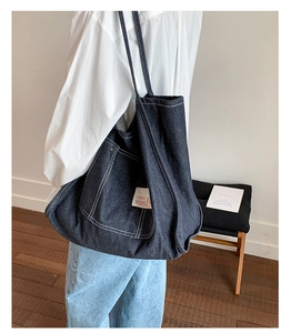 Detailed close-up of dark blue denim tote bag with contrast stitching and front pocket