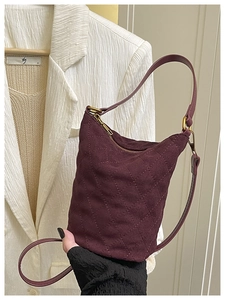 Détail d'un sac seau matelassé bordeaux montrant la texture suède et les dorures