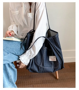Detailed view of deep blue denim tote bag featuring white contrast stitching and logo tag