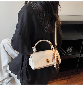 Detail view of white faux leather handbag featuring a vintage gold twist lock and bead charm