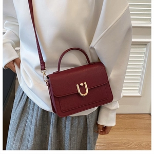 Close-up of burgundy leather crossbody bag with golden metal U-shaped buckle detail