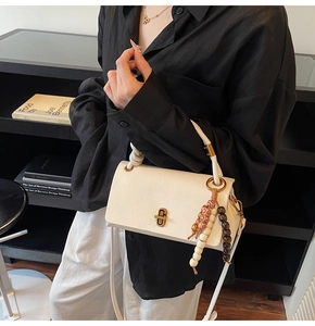 Detail of white leather crossbody bag with golden clasp and tricolor wooden beads