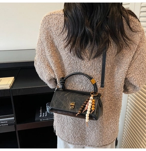Detail view of a black pleated leather handbag with a metal twist lock and bead tassel