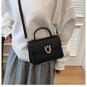 Detail view of black lychee leather handbag with gold U-shaped buckle on a fashion model