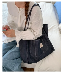 Detail of navy blue denim tote bag featuring white contrast stitching and large front pocket