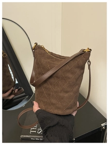 Détail du sac seau en daim marron foncé avec surpiqûres en losange jaunes et fermeture éclair