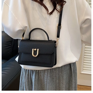 Detail of black litchi grain leather bag with elegant gold U-shaped metal buckle and handle
