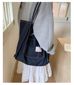 Detail shot of navy denim tote bag with white contrast stitching and side woven label