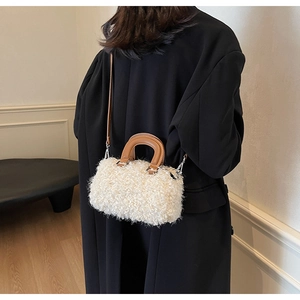 Detail of cream sherpa boston bag with brown leather handles on a black coat