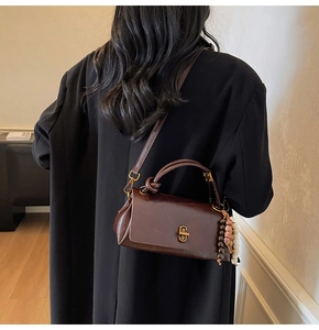 Detailed view of deep brown leather handbag with metal chain lock and decorative beads