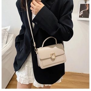 Detail of a beige pebbled leather handbag with a gold U-shaped metal buckle and top handle