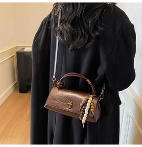 Detail of a brown leather handbag with gold twist handle and beaded tassel charm accessory