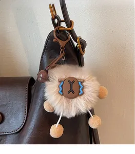Detail of a beige plush monster bag charm with brown metal clip on a leather tote