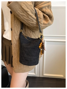 Détail du sac seau matelassé noir avec texture mate et pompon en perles de bois