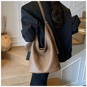 Brown litchi grain leather bucket bag shown as a shoulder bag on a model in a minimal setting