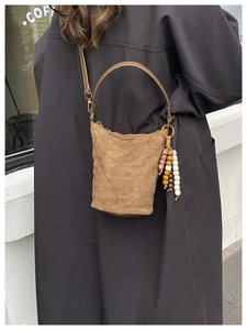 Gros plan sur un sac seau en daim marron avec motif matelassé et breloque perlée