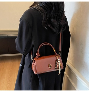 Detail view of a vintage reddish-brown handbag with metal lock and beaded tassel charm