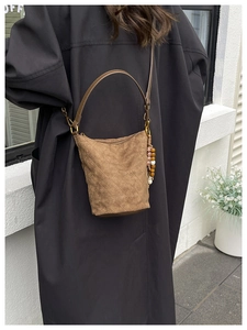 Détail d'un sac seau en daim marron avec surpiqûres en losange et breloque en perles ethniques