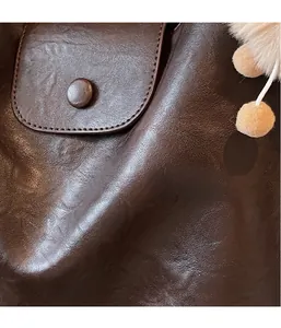 Close-up of brown leather bag with fine stitching and a fluffy beige keychain charm
